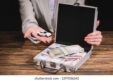 Cropped Shot Of Businesswoman Holding Model Car And Suitcase Safe Box With Russian Rubles On Wooden Table