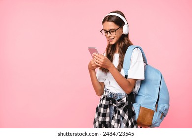 Cropped shot of a caucasian young girl teenager schoolgirl pupil using smart phone while listening to the music in headphones going back to school isolated on pink background. - Powered by Shutterstock