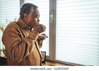 Cropped shot of a contemplative senior man standing alone in his home and enjoying a cup of coffee. Senior Black Man Enjoying a Cup of Coffee at Home.  - Powered by Shutterstock