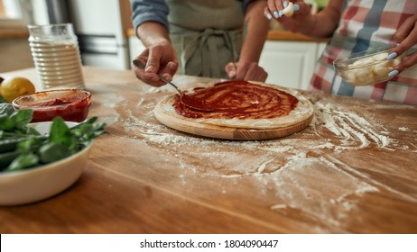 Cropped Shot Of Couple Making Pizza Together At Home. Man In Apron Adding, Applying Tomato Sauce On The Dough While Woman Adding Mozzarella Cheese. Hobby, Lifestyle. Selective Focus. Web Banner