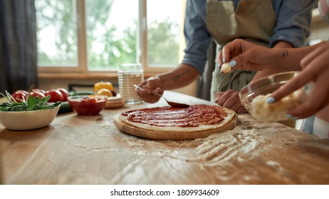 Cropped Shot Of Couple Making Pizza Together At Home. Man In Apron Adding, Applying Tomato Sauce On The Dough While Woman Adding Mozzarella Cheese. Hobby, Lifestyle. Selective Focus. Web Banner