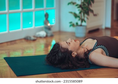 Cropped shot of a dark haired curly girl lying on a yoga mat and taking a rest after the practice. Having her eyes closed while her mouth are slightly open with concentration on breathing.Copy space. - Powered by Shutterstock