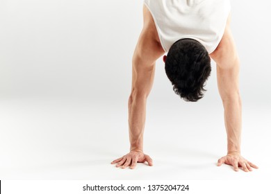 Cropped shot of dark-haired hip hop dancer doing handstand upside down with streched out arms over white studio background