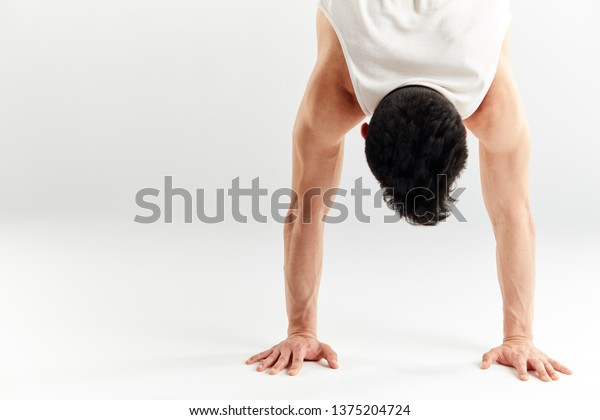 Cropped\
shot of dark-haired hip hop dancer doing handstand upside down with\
streched out arms over white studio\
background