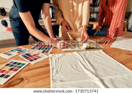 Cropped shot of designers drawing sketches, while creating logo and design of T-shirt. Young man and women working together at custom T-shirt, clothing printing company. Horizontal shot