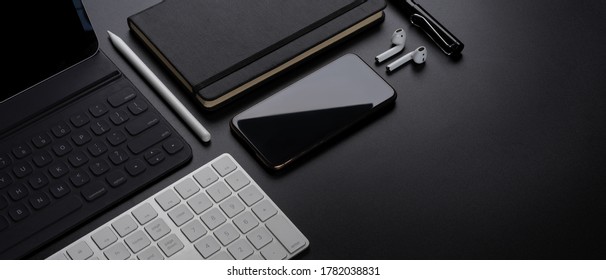 Cropped shot of digital devices with smartphone, tablet, keyboard, stationery, accessories and copy space on dark table