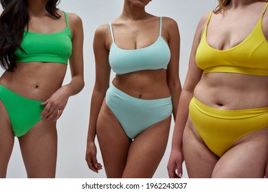 Cropped shot of diverse young women in colorful underwear posing together isolated over light background. Body positivity concept. Horizontal shot
