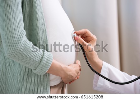 Cropped shot of doctor with stethoscope listening belly of pregnant woman 