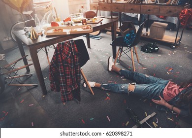 Cropped shot of drunk young woman lying on floor in messy room after party 