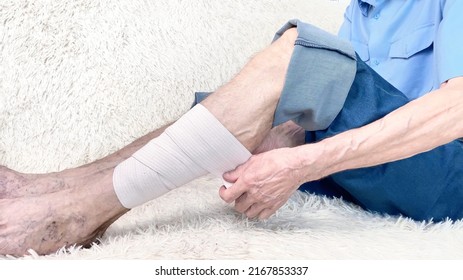 Cropped Shot Of Elderly Man Sitting On Sofa And Suffering From Leg Pain. Leg With Bandage. Bone Disease Or Varicose