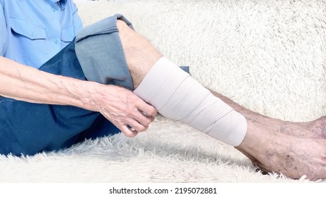 Cropped Shot Of Elderly Man Sitting On Sofa And Suffering From Leg Pain. Leg With Bandage. Bone Disease Or Varicose