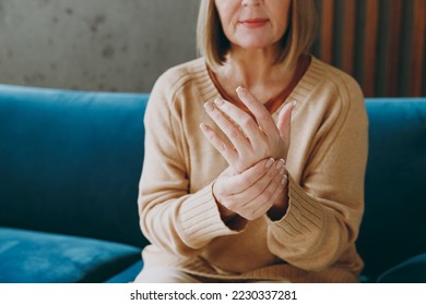 Cropped shot elderly woman 50s years old wearing casual clothes sits on blue sofa do self hand massage rub arm palm stay at home flat rest relax spend free spare time in living room indoor grey wall - Powered by Shutterstock