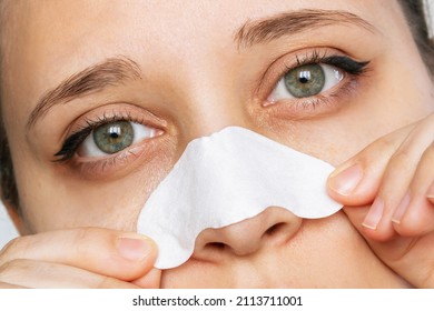 Cropped shot of the face of a woman cleaning the skin of her nose with strips from blackheads or black dots and looking down isolated on a white background. Acne problem, comedones. Close-up