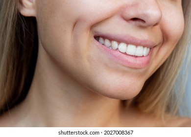 Cropped shot of a face of a young caucasian smiling blonde woman with dimples on her cheeks. Close-up of a blonde girl with even white teeth. Dentistry concept