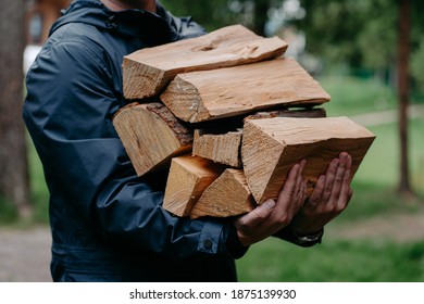 Cropped shot of faceless man in black jacket carries pile of firewood poses against blurred forest background. - Powered by Shutterstock