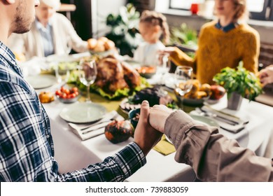 cropped shot of family holding hands and praying on thanksgiving before holiday dinner