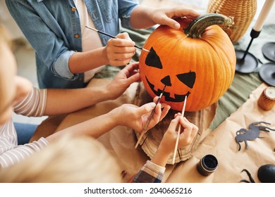 Cropped shot family parent and little kids preparing for holiday Halloween  hands mother and children drawing scary face and paint brushes together pumpkin for house decoration