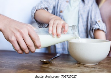 Cropped Shot Of Father With Child Pouring Milk In Bowl For Breakfast