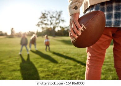 Cropped shot of father holding an oval brown leather rugby ball while playing with his wife and kids in park. Family and kids, nature concept. Horizontal shot - Powered by Shutterstock