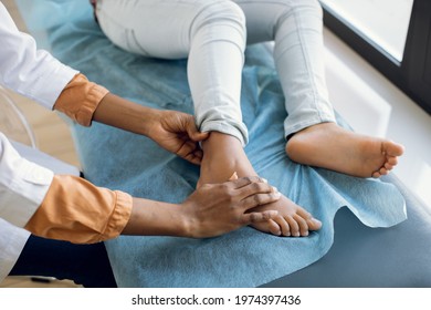 Cropped shot of female afro doctor examining childs feet in hospital. Surgeon, traumatologist or orthopedist doing palpation of little girl leg and foot