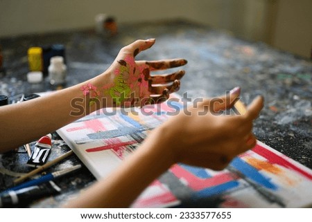 Cropped shot of female artist with dirty hands painting with paintbrush and watercolors on canvas