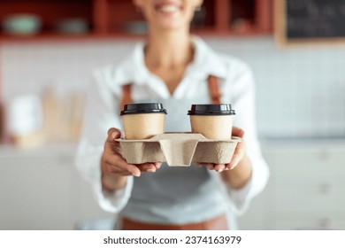 Cropped shot of female barista holding holder with hot takeaway drinks in cafe interior, closeup. Small business concept - Powered by Shutterstock