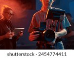 Cropped shot of female cameraman operating equipment in studio set with neon lights copy space