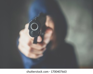 Cropped shot of female criminal (or thief) wearing hood and aiming handgun to the target. Conceptual of a person who commits a crime or force someone to do something against their will with weapon.