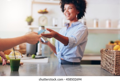 Cropped shot of female employee taking payment from customer, focus on female hands giving credit card for juice bar payment.