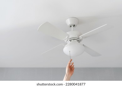 cropped shot of female hand pull switch of ceiling fan with lamp on white background with copy space, room cooling and ventilation concept - Shutterstock ID 2280041877