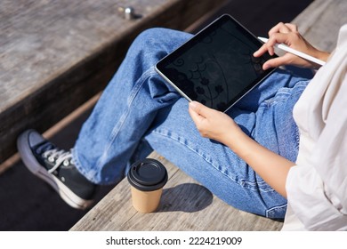Cropped shot of female hands drawing on digital graphic tablet with pen, sitting with cup of coffee outdoors on bench. - Powered by Shutterstock