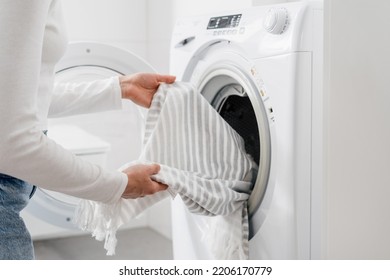 cropped shot of female hands put bed linen or cotton towel in automatic washing machine with open door in bathroom, housekeeping duties