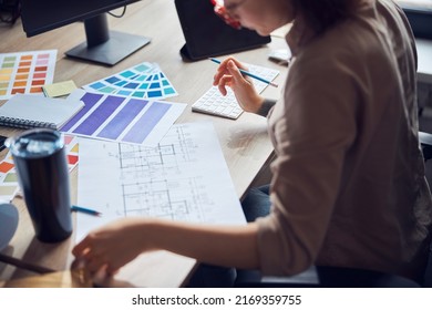 Cropped Shot Of Female Interior Designer Working On A Project With Bluepint And Color Samples, Sitting At The Desk In Her Office