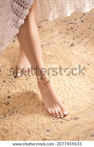 Cropped shot of female legs wearing ankle bracelets made of golden chains with an insert saying 