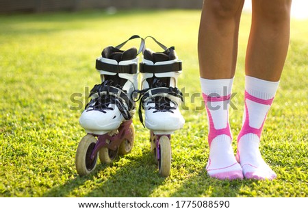 Cropped shot of female legs in white and pink socks and white black roller skates on green grass with sun light. Summer sports. Healthy lifestyle. Activity