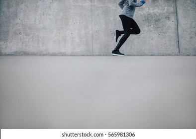 Cropped Shot Of Female Runner Running On Gray Background. Fitness Woman Jogging On Sidewalk In City.