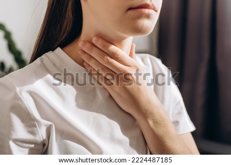 Cropped shot of female suffering from pain sitting on sofa at home. Healthcare and medical concept. Unhealthy sad young caucasian woman with sore throat inflamed tonsils from influenza symptoms