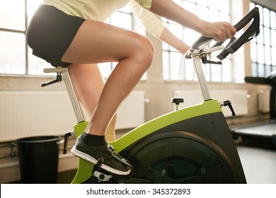 Cropped Shot Of Fitness Woman Working Out On Exercise Bike At The Gym. Female Exercising On Bicycle In Health Club, Focus On Legs.