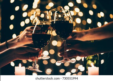 Cropped shot of four people clinking glasses with red wine in front of bokeh background