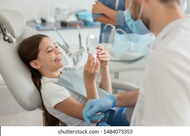 Cropped shot of girl looking in the mirror after dental procedure while mother standing near her for support
