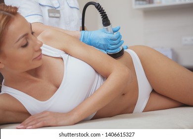 Cropped shot of a gorgeous woman with sexy body getting lifting body treatment by cosmetologist. Beautician using hardware cosmetology machine on a female client, doing ultrasound cavitation