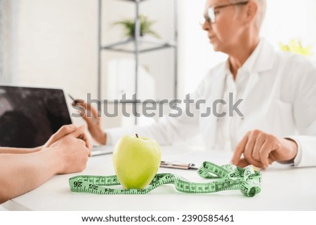 Cropped shot of green apple and measuring tape on dietitian desk. Healthy balanced diet eating concept. Caucasian elderly senior female doctor nutritionist female patient good nutrition habits.