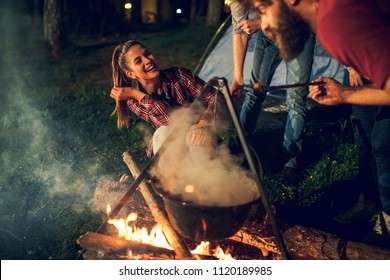 Cropped shot of a group of friends cooking dinner over a campfire while camping in the woods.