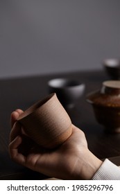 Cropped shot of a hand holding brown teabowl. Cup with ribbed textured surface is made in classic Japanese style. Equipment for tea ceremony is located in the background.  - Shutterstock ID 1985296796