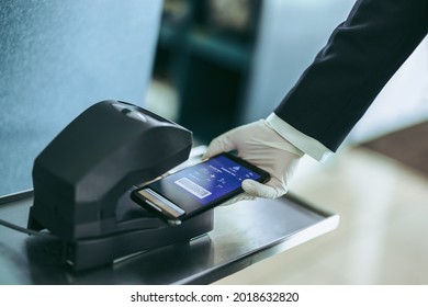 Cropped Shot Of Hand Putting Boarding Pass On Cell Phone Under Scanner At Airport Counter. Hand Of Airport Staff With Hand Glove Scanning Boarding Pass During Pandemic.