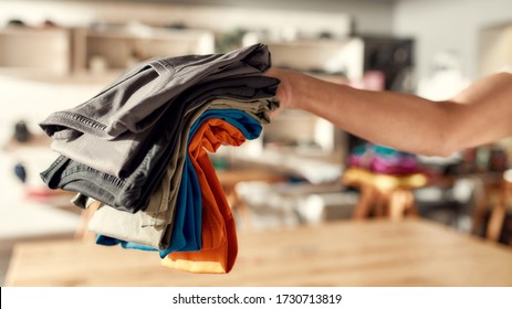 Cropped Shot Of Hand Of Woman Holding Stack Of Colorful T Shirts While Standing In The Store. Clothes At Custom T-shirt, Clothing Printing Company. Horizontal Shot