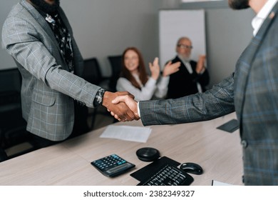 Cropped shot handshaking of unrecognizable African-American and Caucasian businessmen partner after signing contract at group negotiations getting team applause, successful business deal, closeup. - Powered by Shutterstock