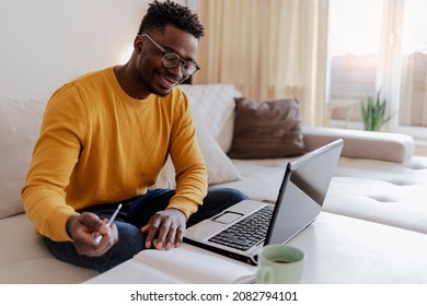 Cropped Shot Of A Handsome Young Businessman Sitting Alone In His Home Office And Working On Laptop Computer At Home. Smiling Black Man Using Laptop In Living Room. Businessman Using Laptop At Home.