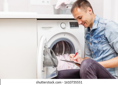 Cropped Shot Of Handyman With Toolbelt And Clipboard Checking Washing Machine In Bathroom