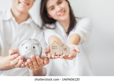 Cropped Shot Of Happy Asian Couple Holding Piggy Bank And Wooden House Models. Saving Money For Buying New House Concept